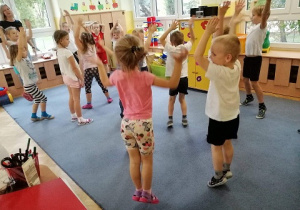Dzieci z grupy biedronki przebrane w stroje gimnastyczne ćwiczą skakanie pajacyków